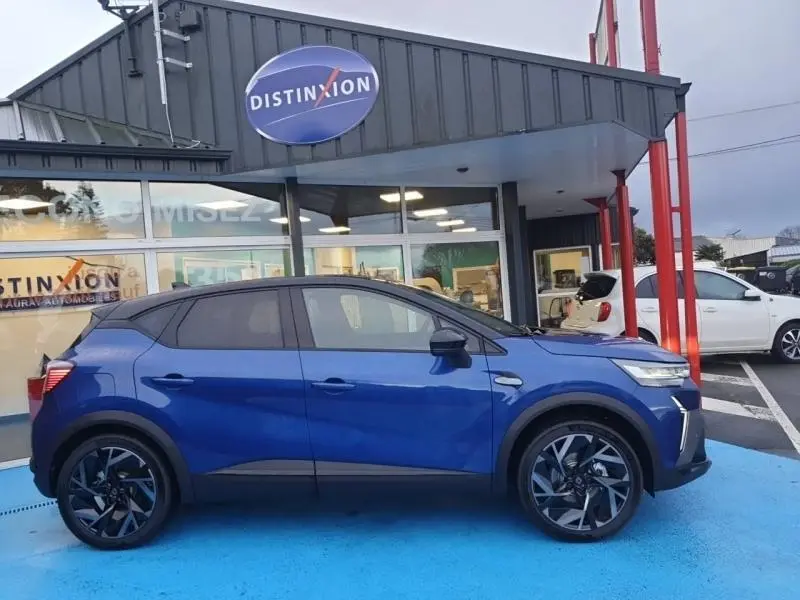 Profil côté gauche du Renault Captur 2025 Bleu Iron esprit Alpine avec jantes alu et toit noir, stationné devant un showroom.