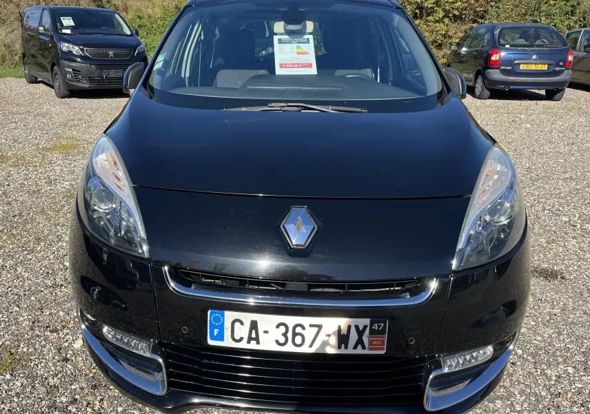 Vue avant d'une Renault Scénic III noire de 2012, avec calandre chromée et plaques d'immatriculation françaises visibles.