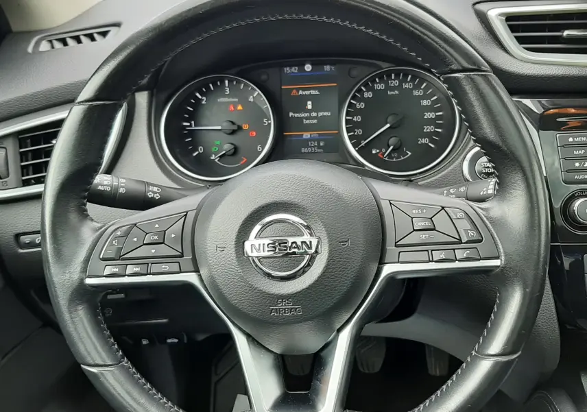 Vue rapprochée du volant en cuir noir d'un Nissan Qashqai 2020, avec tableau de bord et affichage digital au centre.