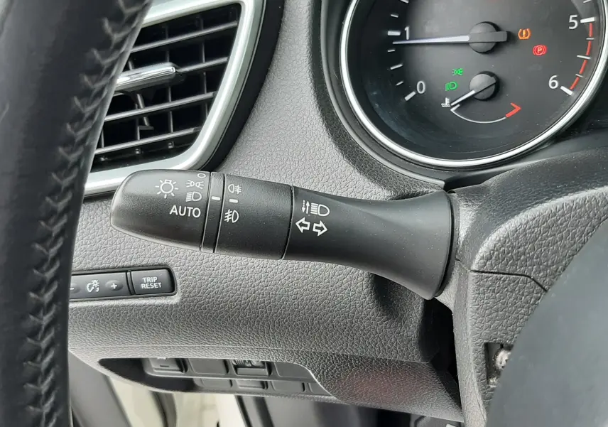 Gros plan sur la commande des feux et clignotants à gauche du volant dans l'habitacle noir du Nissan Qashqai blanc 2020.