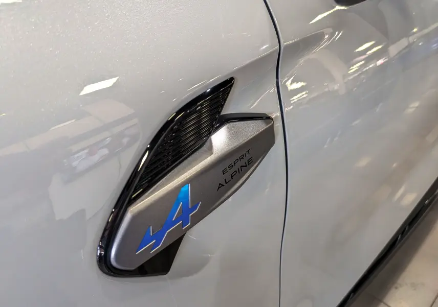 Gros plan sur l'aile avant gauche gris Rafale du Renault Symbioz E-TECH avec logo Alpine bleu et inscription Esprit Alpine.