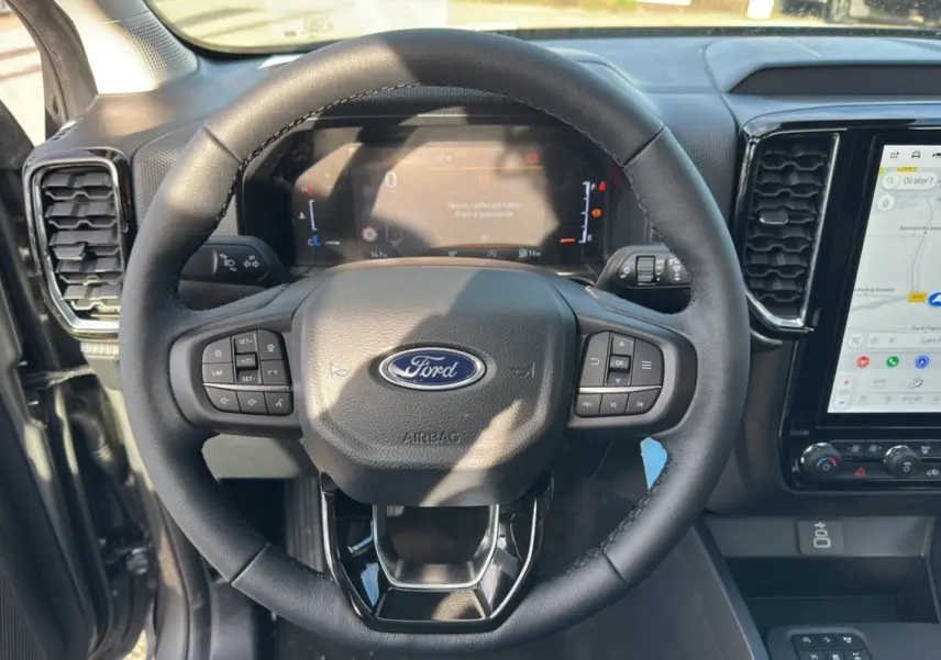 Vue rapprochée du volant cuir multifonctions Ford Ranger 2025 avec tableau de bord numérique et écran tactile GPS.