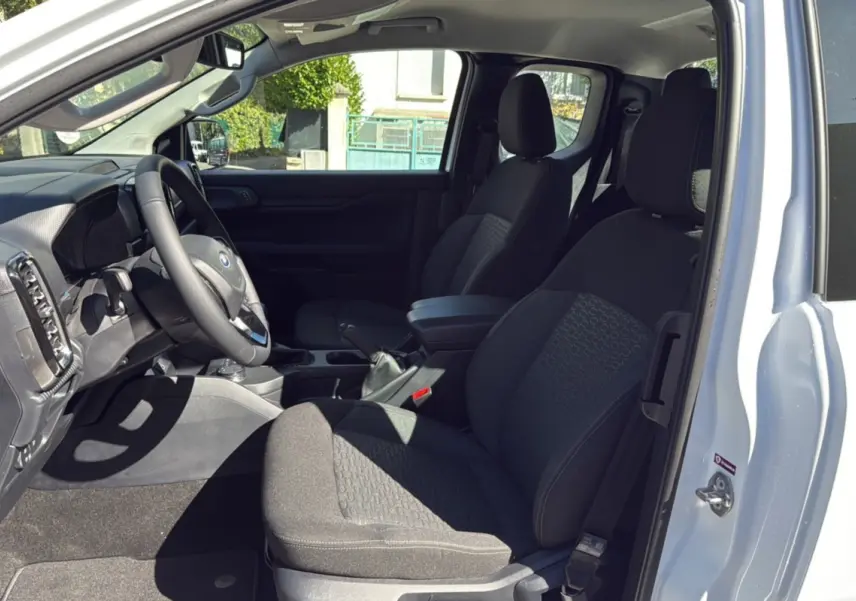Vue intérieure côté conducteur du Ford Ranger blanc glacier 2025, montrant les sièges noirs et le volant multifonctions en cuir.