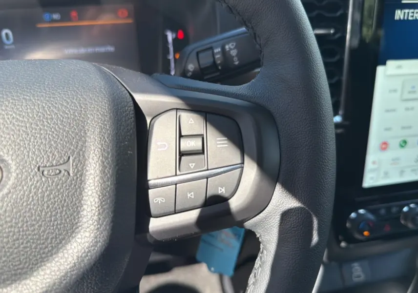 Gros plan sur le volant cuir multifonctions du Ford Ranger blanc glacier, avec commandes audio et écran tactile en arrière-plan.