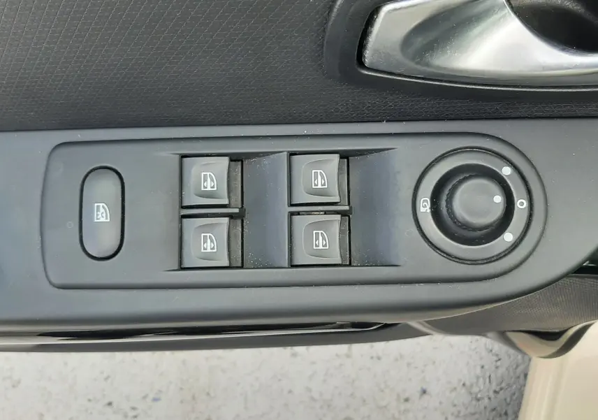 Vue rapprochée des commandes de lève-vitres et rétroviseurs sur la porte avant gauche d'une Renault Clio IV beige.