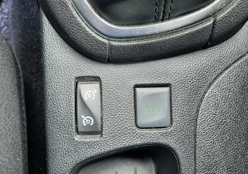 Gros plan sur les commandes du mode ECO et régulateur de vitesse près du levier de vitesses d’une Renault Clio IV beige.
