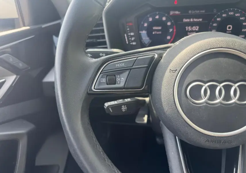 Vue rapprochée du volant cuir noir d'une Audi A1 Sportback 2025 avec commandes intégrées et cockpit numérique en arrière-plan.