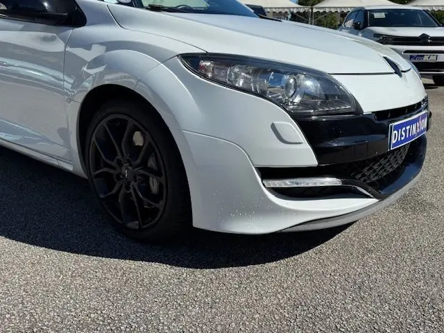 Vue 3/4 avant droite d'une Renault Mégane III Coupé RS blanche nacrée avec jantes noires et phares Xenon.