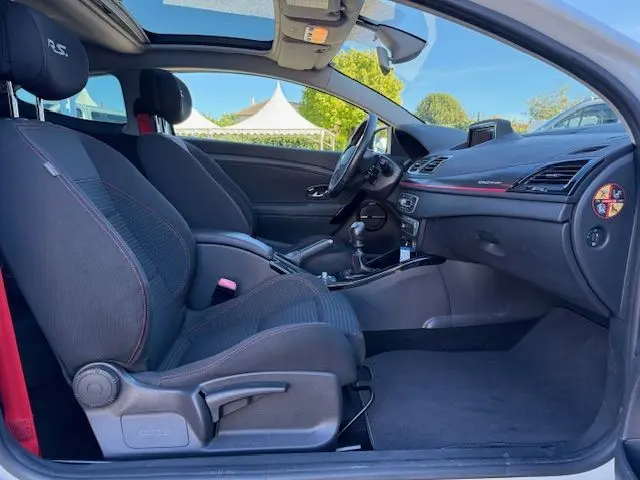 Intérieur côté conducteur de Renault Mégane III Coupé 2.0T RS blanc nacré, sièges tissu noirs avec surpiqûres rouges et toit ouvrant.