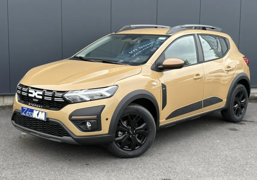 Vue 3/4 avant droite d'une Dacia Sandero Stepway beige Safari avec jantes noires et barres de toit gris Mégalithe.