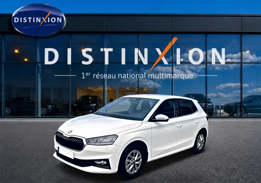 Vue 3/4 avant droite d'une Skoda Fabia blanche 2025 devant une vitrine avec logo Distinxion.