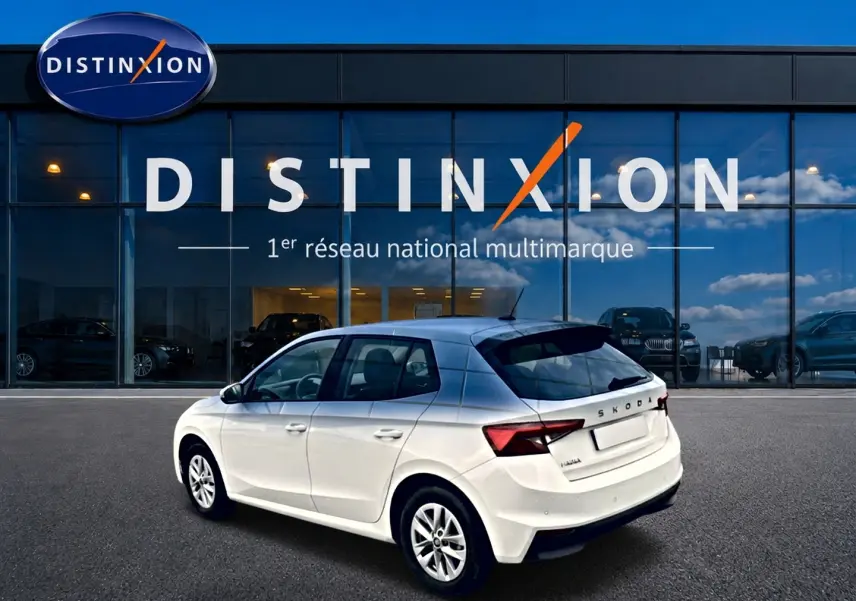 Vue 3/4 arrière droite d'une Skoda Fabia blanche 2025 garée devant une vitrine Distinxion.