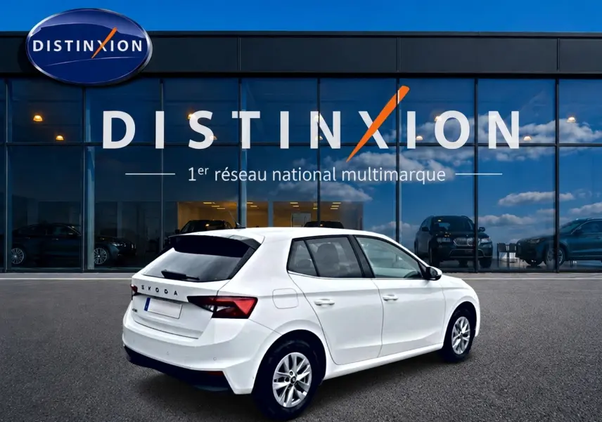 Vue 3/4 arrière droite d'une Skoda Fabia blanche 2025 avec jantes alu, stationnée devant un showroom Distinxion.