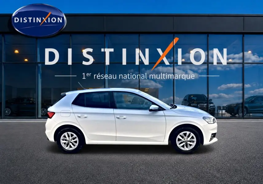 Vue latérale droite d'une Skoda Fabia blanche 2025 garée devant une vitrine avec logo Distinxion.