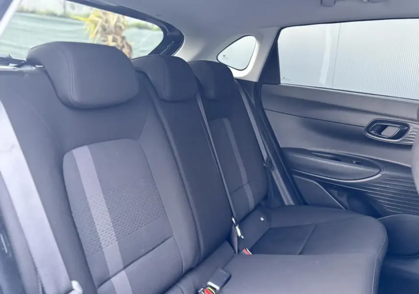 Vue intérieure côté droit des sièges arrière noirs de la Hyundai i20 2025 avec ceinture et garnitures de porte visibles.