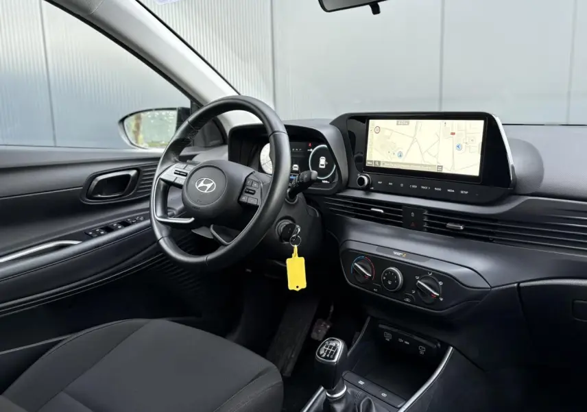 Vue intérieure côté conducteur de la Hyundai i20 2025, volant cuir, écran GPS tactile et levier de vitesses manuel.