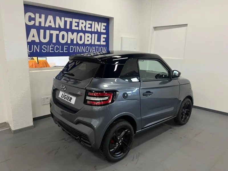 Vue 3/4 arrière droite d'une Ligier JS50 Sport Elite E5+ gris métallisé avec toit noir et jantes noires en intérieur showroom.