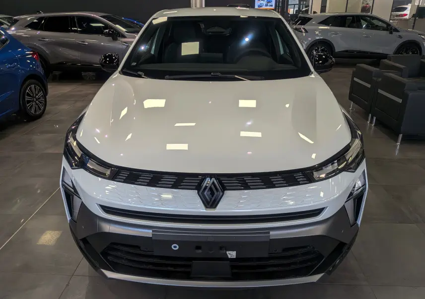 Vue frontale d'une Renault SYMBIOZ blanc nacré en showroom, avec calandre noire et logo Renault central bien visible.
