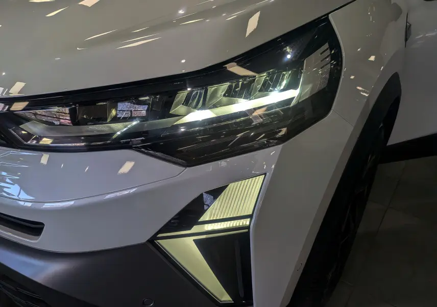 Gros plan sur le phare avant droit du Renault Symbioz blanc nacré, mettant en valeur son design LED moderne et anguleux.