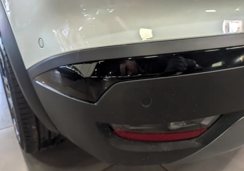 Gros plan sur le pare-chocs arrière gauche blanc nacré du Renault Symbioz E-TECH avec feu antibrouillard et capteur de stationnement.