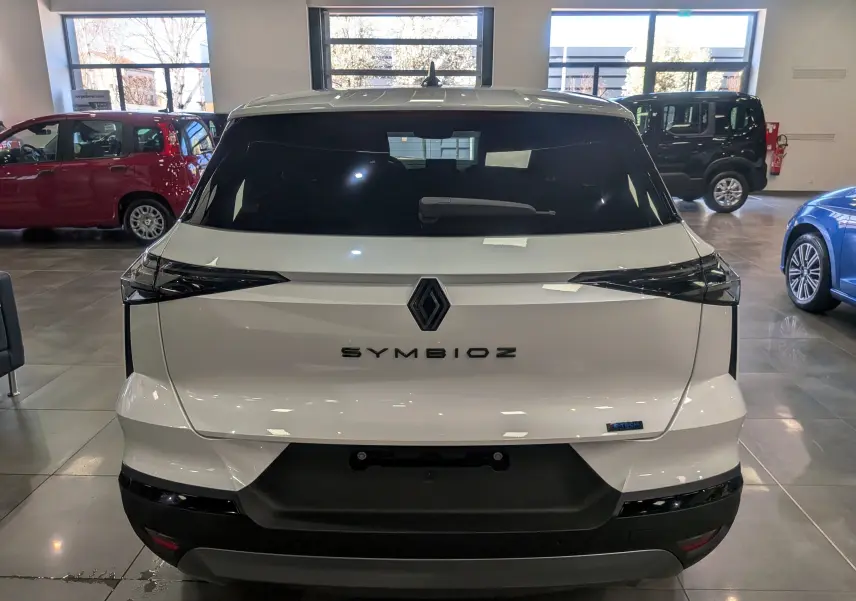 Vue arrière d’un Renault Symbioz blanc nacré en showroom, avec feux arrière noirs et logo central visible.