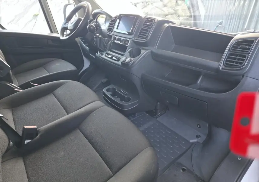 Vue intérieure côté conducteur du Fiat Ducato Fourgon 2023, montrant sièges noirs et tableau de bord avec écran tactile.