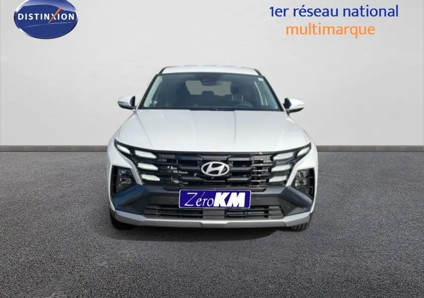 Vue frontale d'un Hyundai Tucson blanc Atlas 2026 avec calandre noire et feux LED distinctifs allumés.
