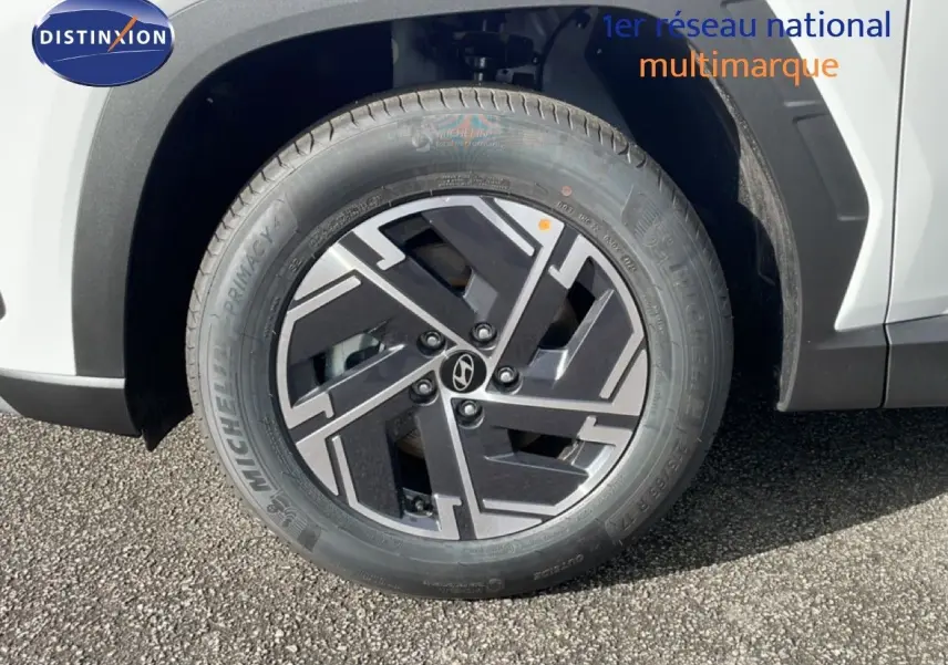 Gros plan sur la roue avant droite d’un Hyundai Tucson blanc Atlas, avec jante alliage noire et grise au design géométrique.