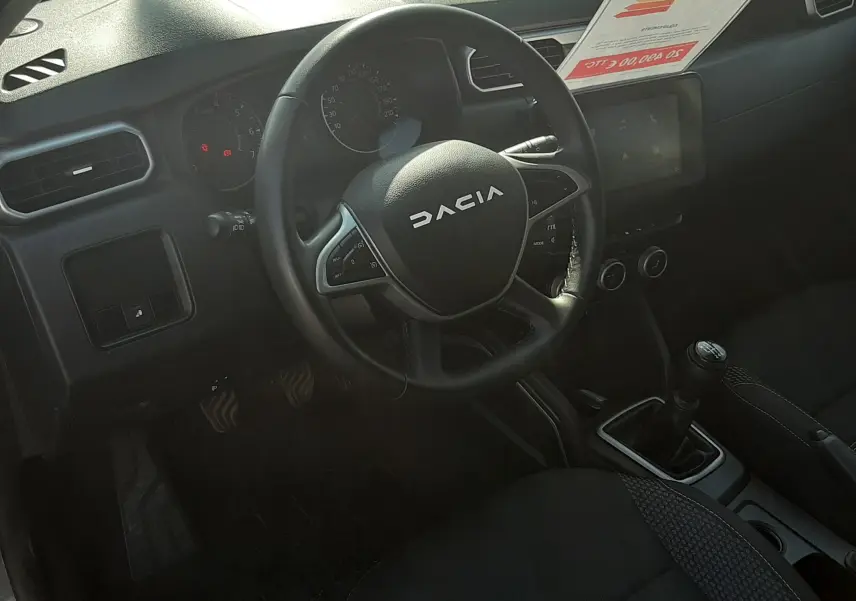 Vue intérieure côté conducteur du Dacia Duster 2024, volant multifonction, tableau de bord noir et levier de vitesses manuel.