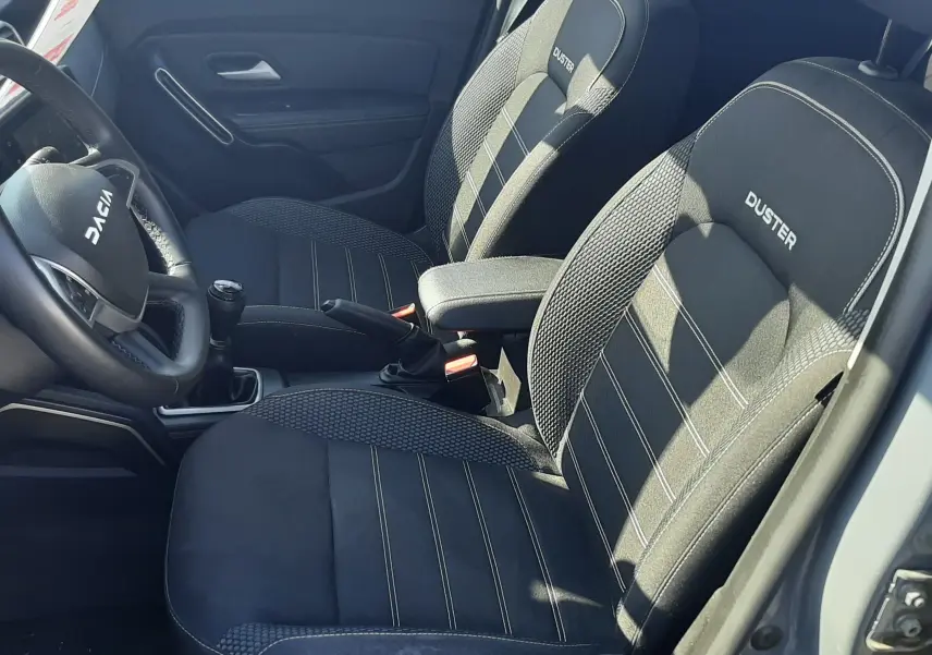 Vue intérieure côté conducteur du Dacia Duster 2024, sièges tissu gris avec logo DUSTER brodé sur appuie-têtes.
