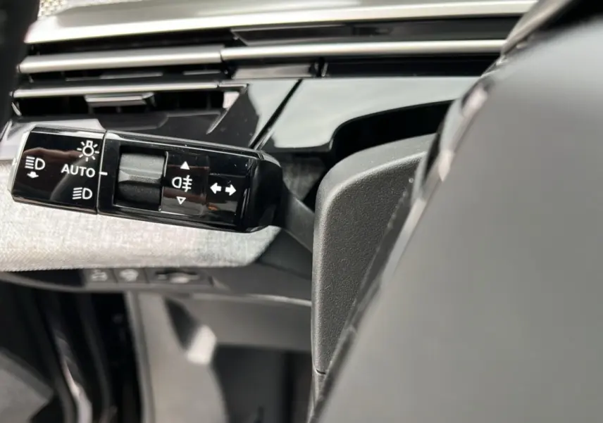 Gros plan sur la commande des feux et clignotants à gauche du volant dans l'habitacle du Peugeot 3008 Hybrid 2025.