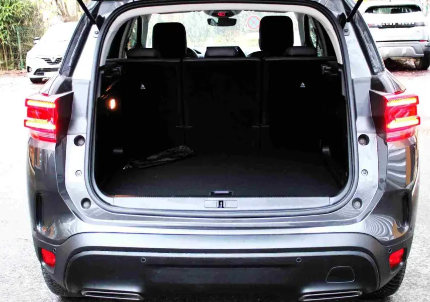 Coffre ouvert d’un Citroën C5 Aircross gris platinium vu de l’arrière, feux arrière allumés et intérieur spacieux.