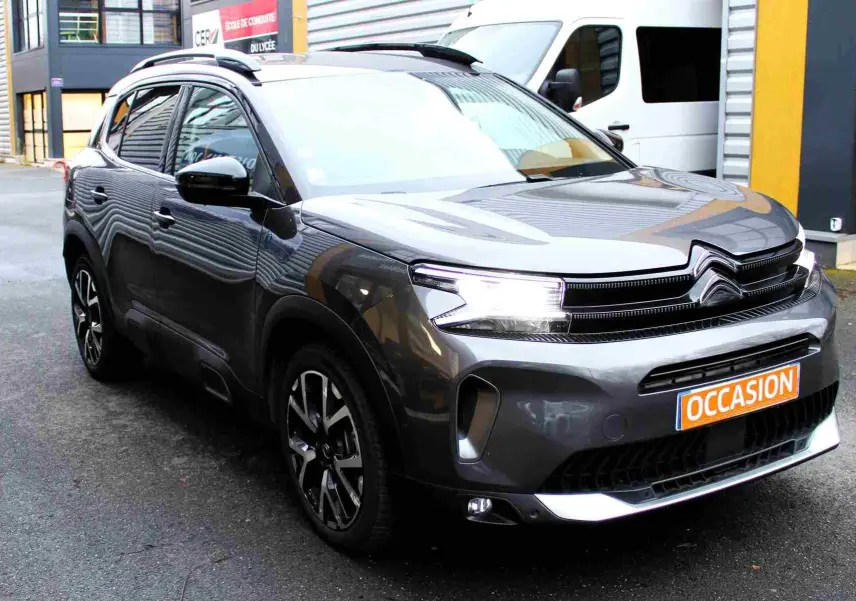 Citroën C5 Aircross gris platinium en 3/4 avant droit avec phares allumés et jantes noires et argentées.