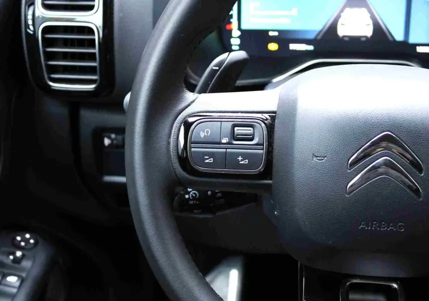 Gros plan sur le volant cuir du Citroën C5 Aircross hybride, avec commandes intégrées et tableau de bord numérique en arrière-plan.