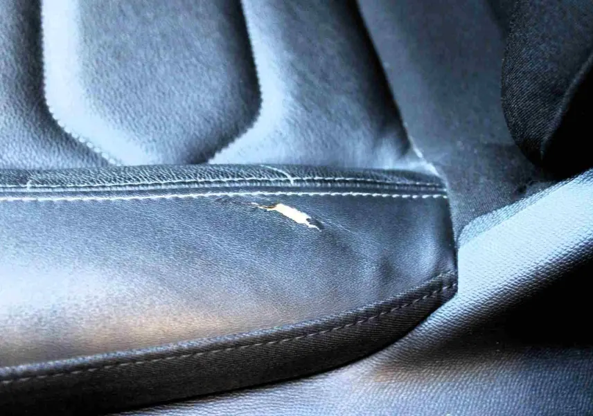Détail en gros plan d'une déchirure sur la sellerie en cuir noir du siège avant d'une Citroën C5 Aircross gris platinium hybride rechargeable.