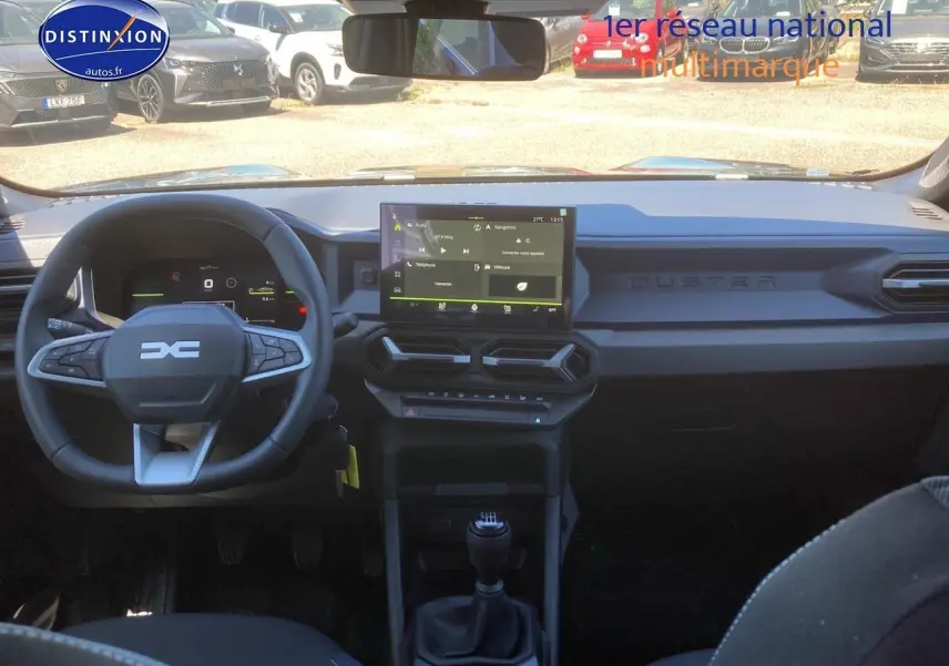 Vue intérieure frontale du tableau de bord noir du Dacia Duster 2025 avec écran tactile et volant multifonction.