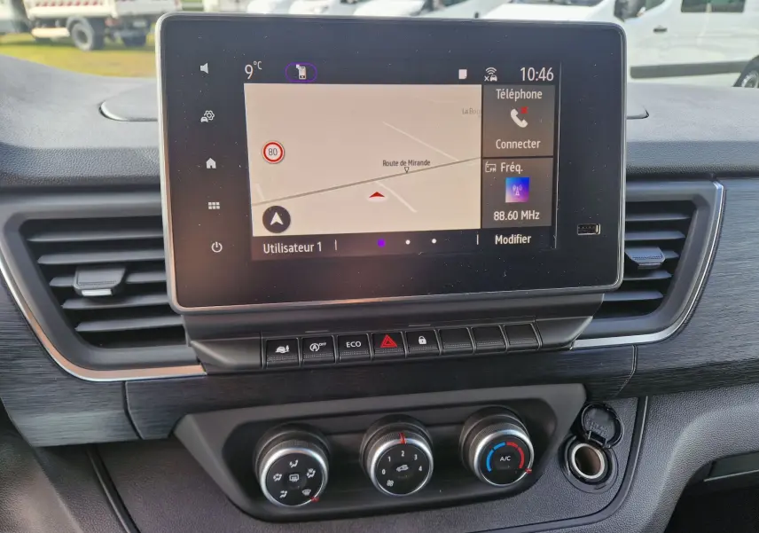 Vue rapprochée du tableau de bord du Nissan Primastar 2025 avec écran tactile affichant la navigation et commandes climatisation.