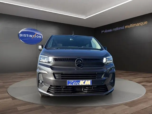 Vue frontale d'un Citroën Jumpy gris titane avec projecteurs LED, présenté en showroom sur un socle circulaire.