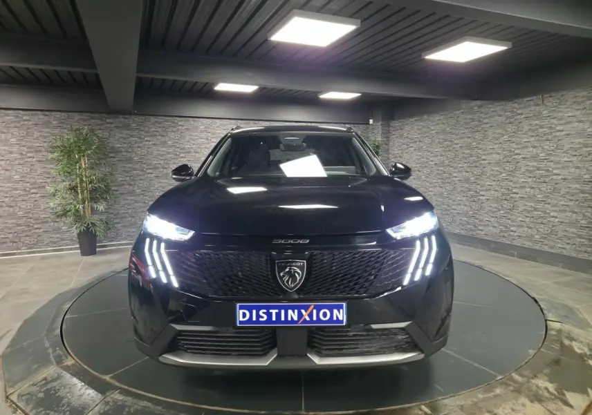 Vue frontale d'un Peugeot 5008 noir 2025 avec feux LED allumés et calandre noire brillante dans un showroom.