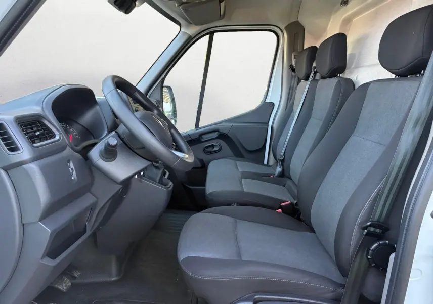 Vue intérieure côté conducteur du Renault Master blanc 2024, montrant les trois sièges en tissu gris et le tableau de bord.