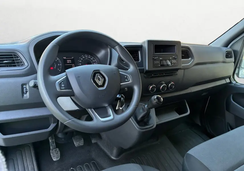 Vue intérieure du poste de conduite du Renault Master 2024, volant noir avec logo, tableau de bord et levier de vitesses manuel.