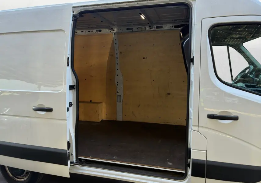 Vue latérale gauche d’un Renault Master blanc 2024 avec porte coulissante ouverte montrant l’intérieur vide en bois.