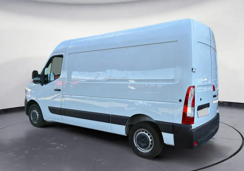 Vue 3/4 arrière gauche d’un fourgon blanc Renault Master L2H2 2024 avec bande noire latérale et feux arrière verticaux.