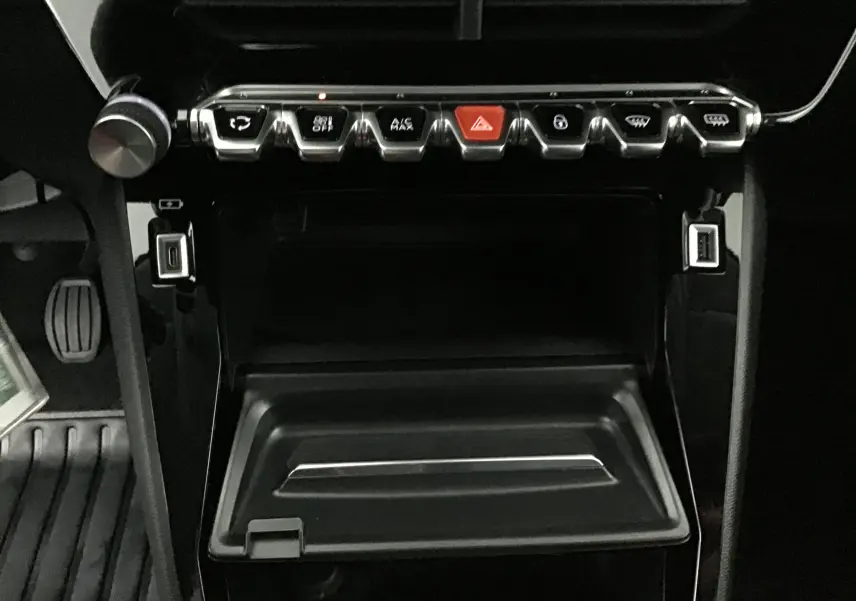 Vue rapprochée du tableau de bord noir de la Peugeot 208 2022, mettant en valeur les commandes chromées et le rangement ouvert.