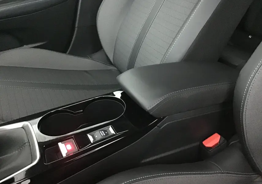 Gros plan sur la console centrale noire et les sièges gris foncé du Peugeot 208 1.2 PureTech 2022 avec accoudoir cuir.