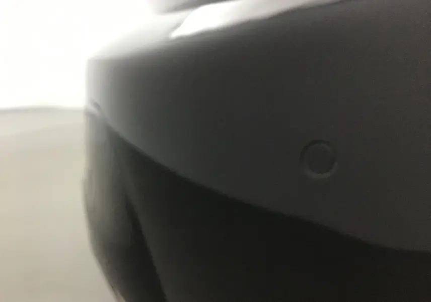 Gros plan sur le pare-chocs avant noir d'une Peugeot 208 2022, mettant en valeur le capteur de stationnement intégré.