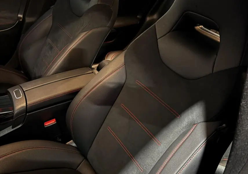 Vue intérieure rapprochée des sièges avant noirs avec surpiqûres rouges du Mercedes CLA 250 e AMG Line blanc 2023.