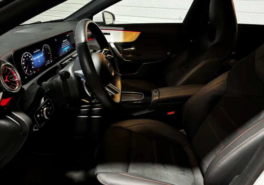 Vue intérieure côté conducteur de la Mercedes CLA 250 e AMG Line 2023, sièges noirs avec surpiqûres rouges et tableau de bord numérique.