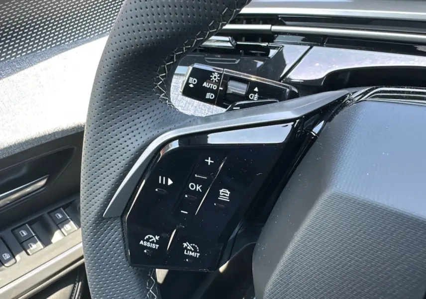 Gros plan sur le volant cuir perforé du Peugeot 3008 Hybrid 145 GT avec commandes multifonctions et bouton assist.