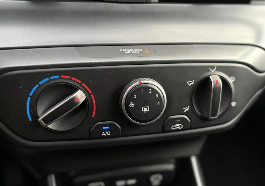 Gros plan sur les commandes de climatisation manuelle noires de la Hyundai i20 Rouge Dragon Metal, avec réglages température et ventilation.